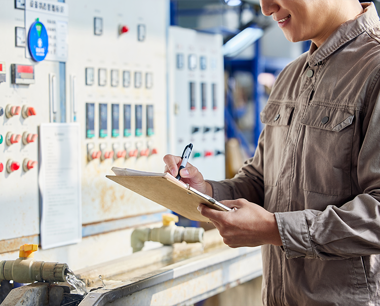 Industrial worker in workwear recording data at a control panel, demonstrating Mingkai Environmental’s customized bag cage service support.